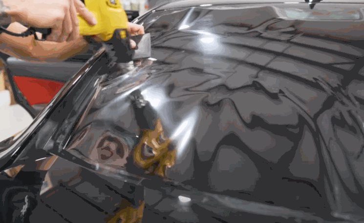 A technician uses a heat gun to shrink window tint film on a car’s rear windshield.