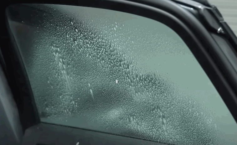 A car door window covered in condensation, showing water droplets across the glass surface.