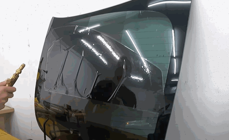 A partially applied window tint film being heat-treated and smoothed over a car’s rear window.