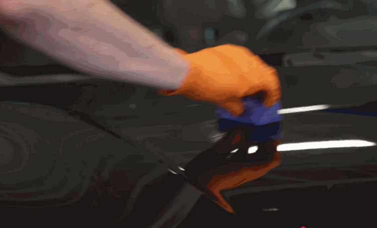 A gloved hand applies ceramic coating to a black car using a blue foam applicator, creating a high-gloss, protective finish.