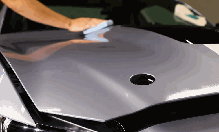 Microfiber cloth buffing the hood of a silver car to smooth and enhance the finish after ceramic coating application.