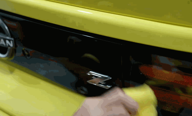 Hand wiping down the rear of a yellow Nissan Z, prepping the surface for ceramic coating by ensuring it’s clean and residue-free.
