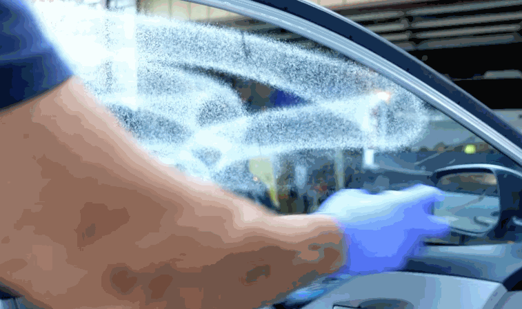 A gloved technician sprays a cleaning solution onto the inside of a car window to prepare it for tint installation.