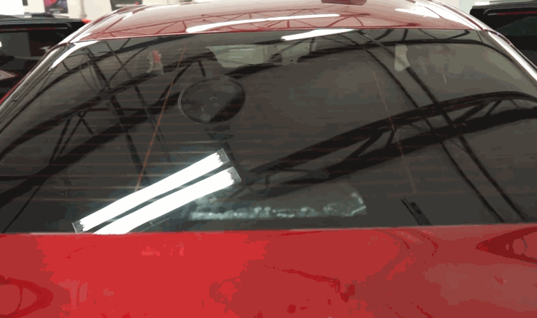 View from outside a red car as the rear windshield tint is installed and smoothed from the inside.