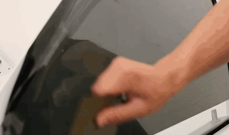 A technician presses and smooths window tint film onto a car’s side window using a squeegee.