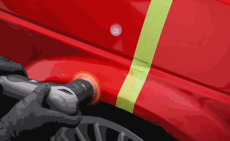 Paint correction in progress on a red car panel using a polishing tool, with tape separating treated and untreated areas for a ceramic coating prep demo.