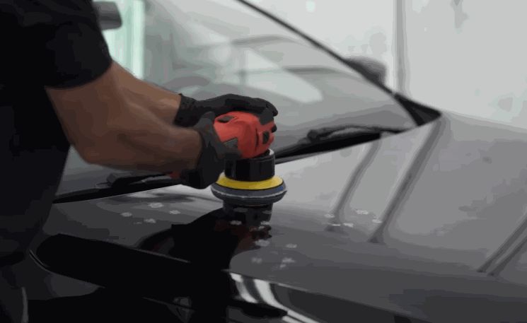 A detailer uses a dual-action polisher on the hood of a black car to prep the surface for ceramic coating by removing swirls and enhancing gloss.