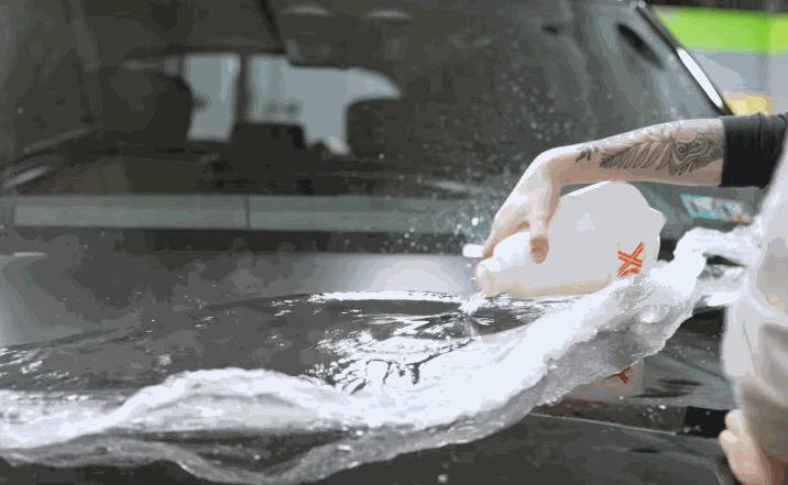 Installer pouring slip solution onto protection film during application on a car hood.