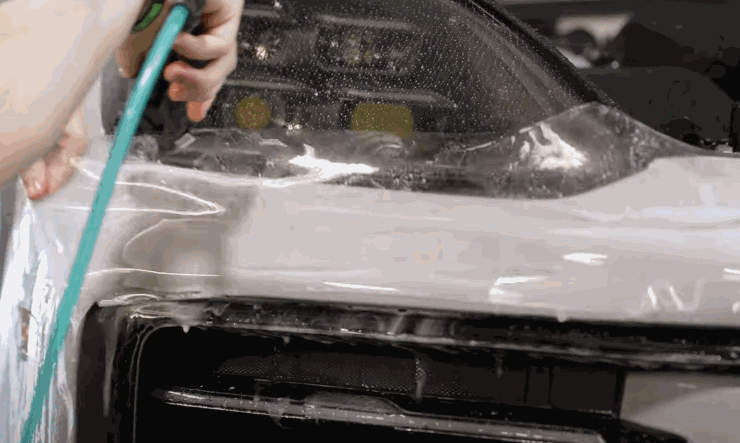 Technician stretching and positioning protection film around a car’s front headlight.