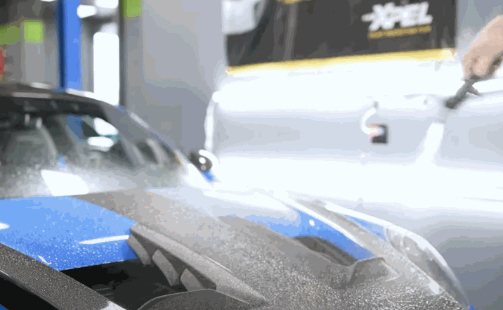 Detailer spraying water over a sports car’s surface before installing protection film.
