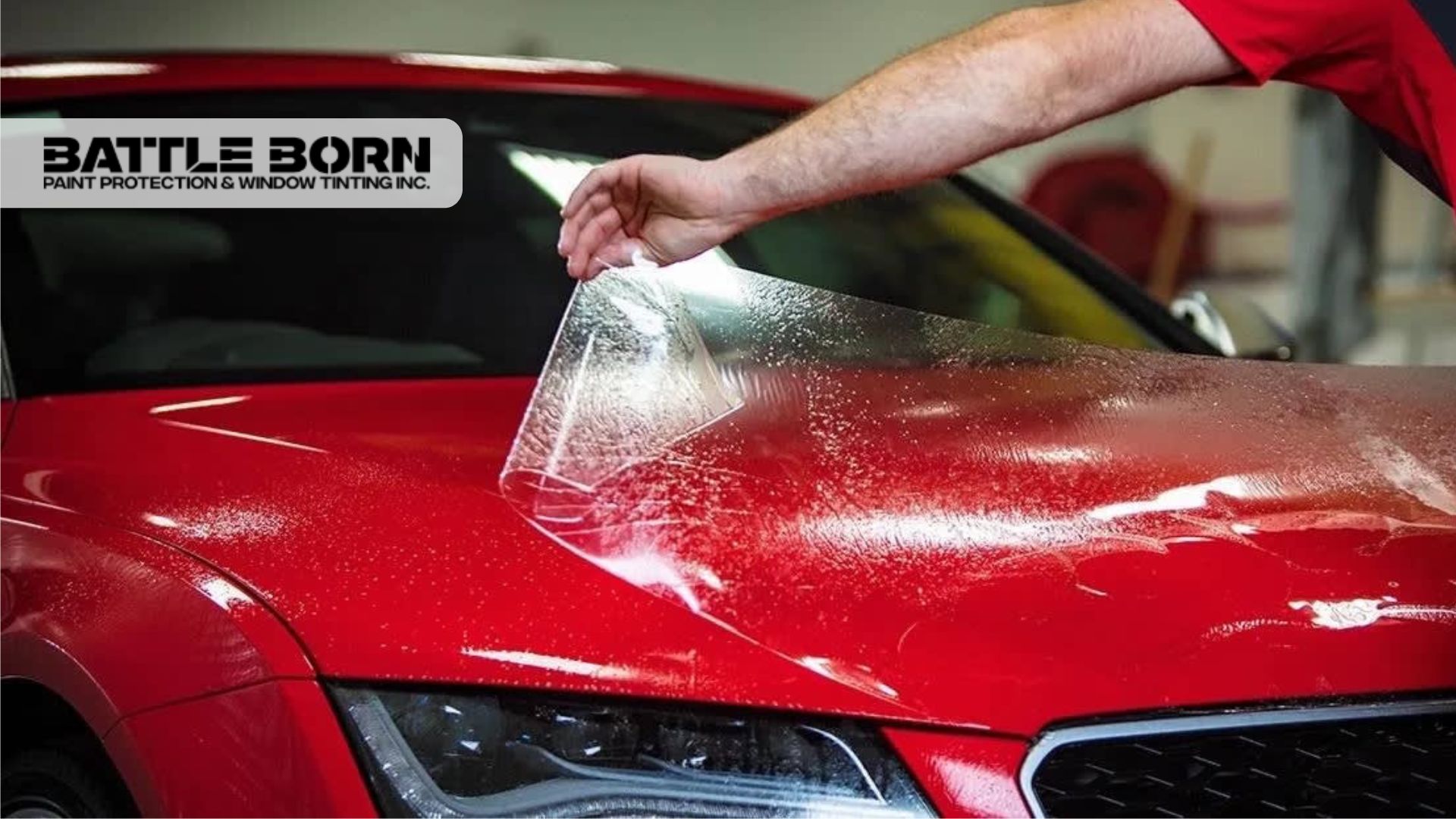 Technician applying clear protection film to the hood of a red sports car for long-lasting paint defense.