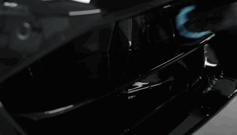 A gloved hand applies ceramic coating inside a black car’s front grille area, ensuring complete surface coverage.