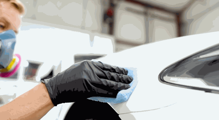 A technician wearing gloves applies ceramic coating to a white car panel using a soft applicator cloth.