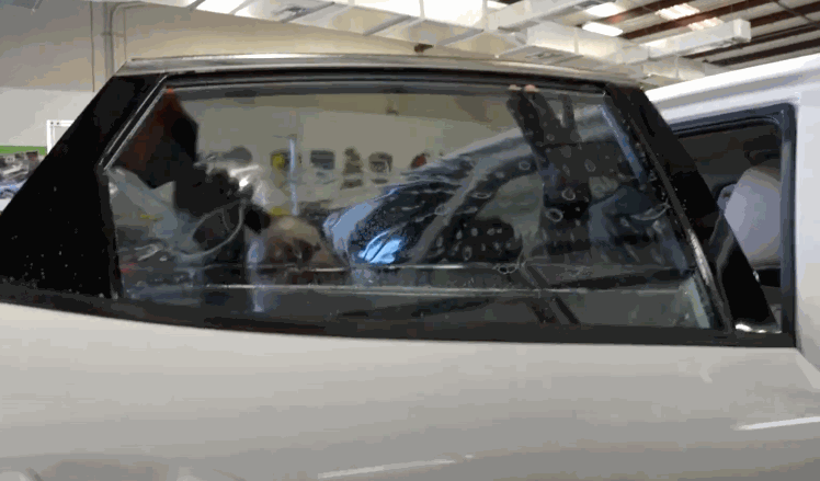 Looped video of a professional smoothing out freshly applied window tint on a side window of a white car inside a shop.