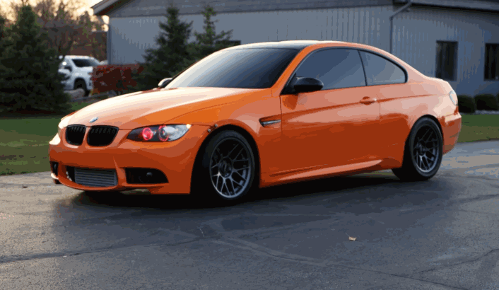A bright orange BMW coupe drives away, its paint gleaming after ceramic coating treatment.