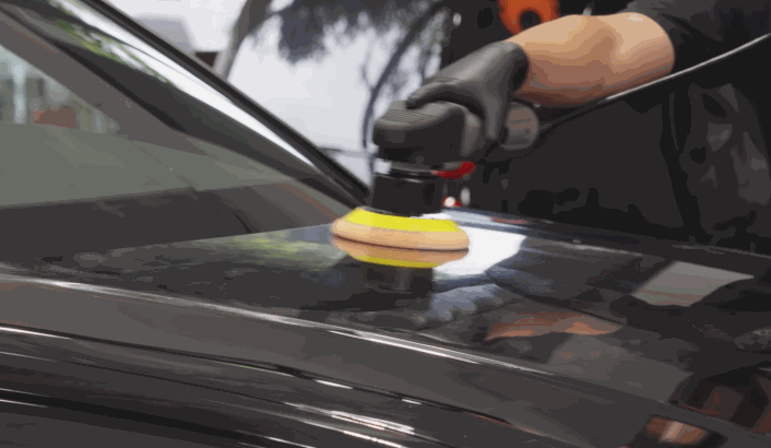 A detailer uses a dual-action polisher to buff wax into a black car’s surface, enhancing its shine temporarily.