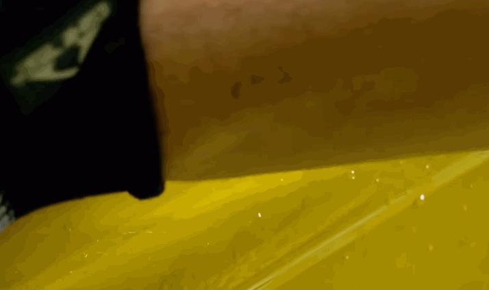 Close-up of a squeegee smoothing yellow paint protection film onto a car panel during installation.