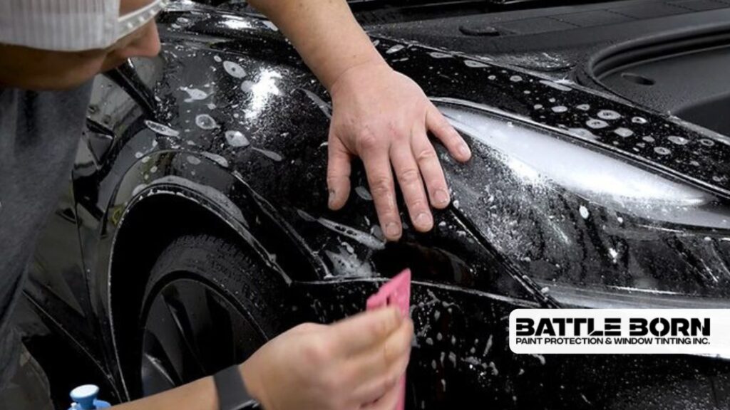 Technician applying clear paint protection film to the fender of a black vehicle, with visible soap and water for smooth adhesion.