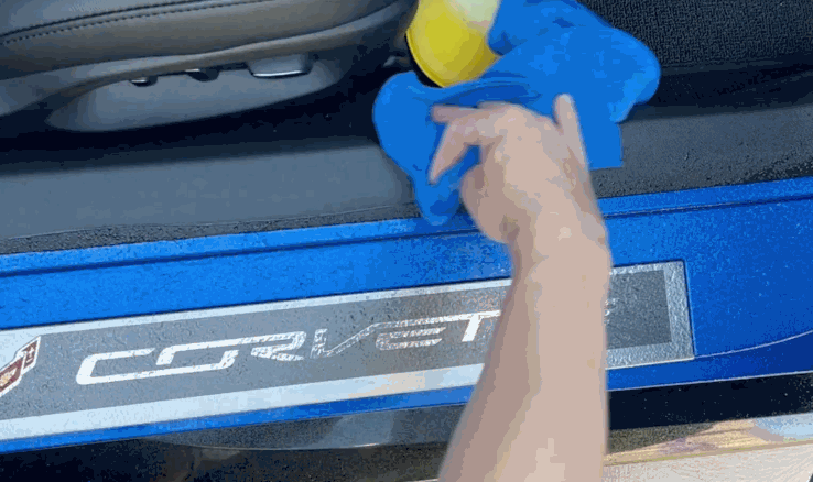 Close-up of a person cleaning the door sill area of a blue Corvette with a microfiber cloth before applying paint protection film.