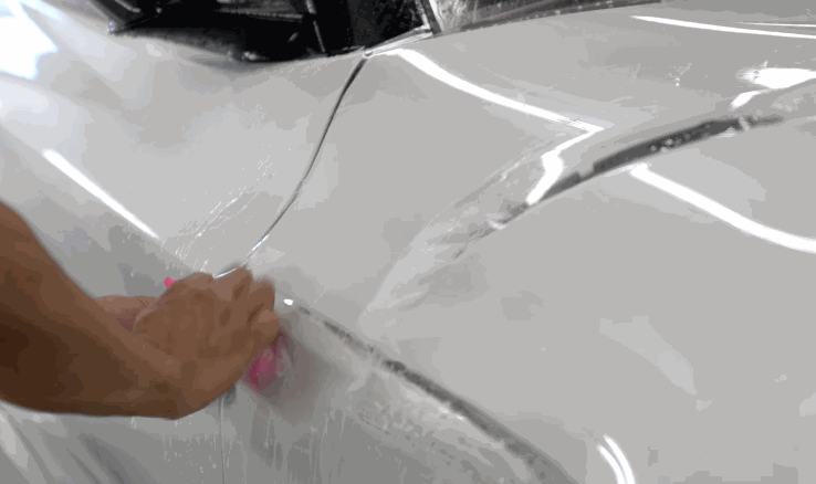 Installer uses a squeegee to press paint protection film onto the side panel of a white vehicle.
