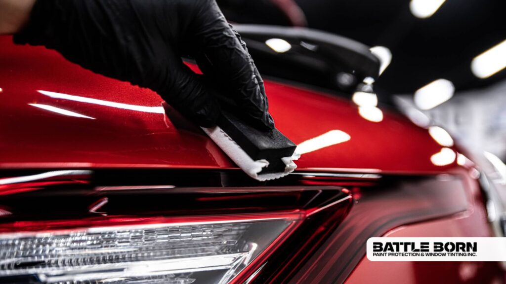 Close-up of a gloved hand applying ceramic coating to a red car’s taillight area using a foam applicator block.