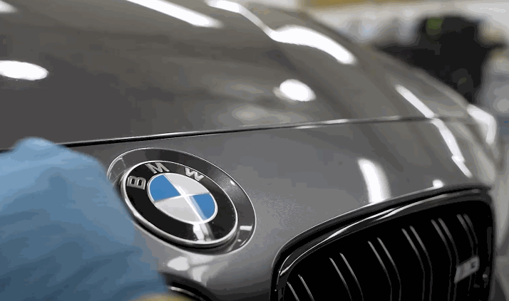 A gloved hand wipes down the hood of a BMW after ceramic coating, revealing a mirror-like gloss and clean finish.