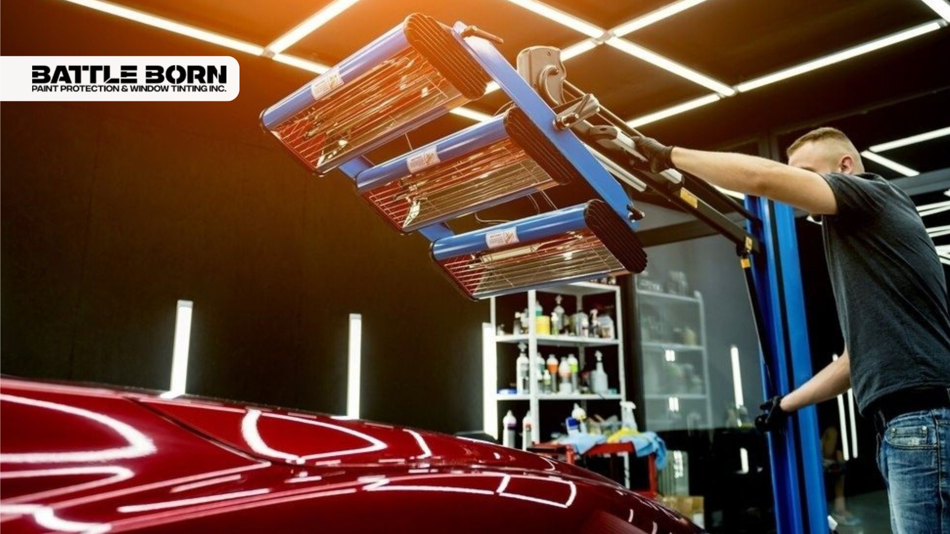 Technician using infrared curing lamps on a red car's surface inside a detailing studio, part of the ceramic coating application process.