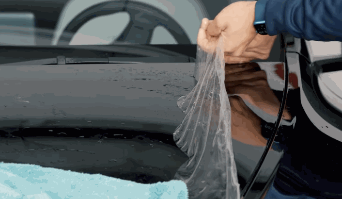 A technician carefully peels off old paint protection film from the surface of a black car during a replacement process.