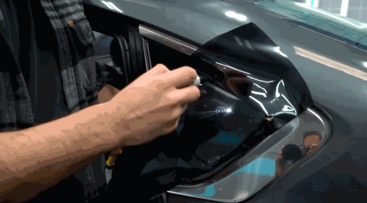 Close up of a technician using a tool to press and shape window tint film inside a car door frame. The glossy black film is carefully adjusted to fit the contours of the window. This step ensures a clean and seamless window tint installation.